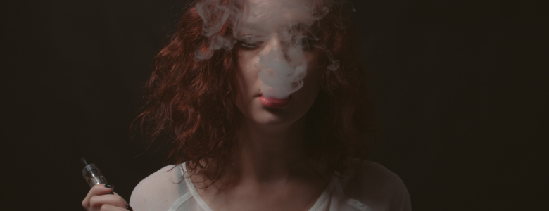 Young red head blows e-cigarette smoke into her face