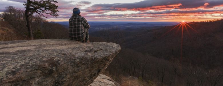 A person sits atop a mountain in Virginia overlooking the landscape and a beautiful sunset